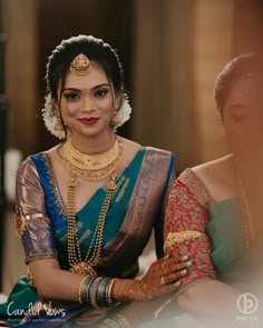 a woman in a green and gold sari sitting down with her hands on her chest