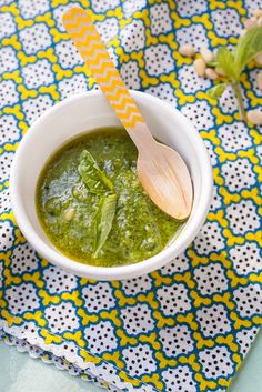 a white bowl filled with pesto next to a wooden spoon on top of a blue and yellow napkin