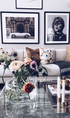 a living room with pictures on the wall and flowers in a vase sitting on a coffee table