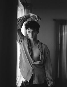 black and white photograph of a shirtless man leaning on a window sill with his hands behind his head