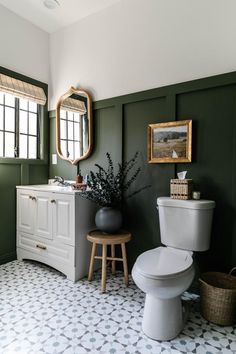 a white toilet sitting next to a bathroom sink under a mirror on top of a wall