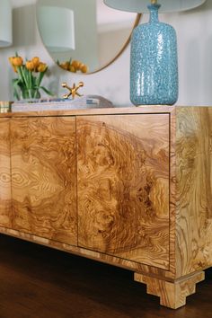 a blue vase sitting on top of a wooden sideboard next to a lamp and mirror