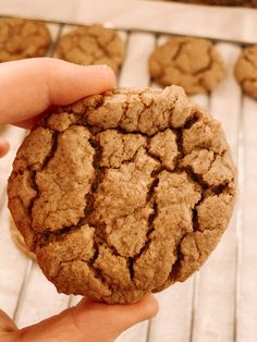 a person holding a cookie in their hand on top of a rack with more cookies behind it