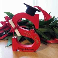 a graduation cap and tassel on top of a red wooden letter with greenery in the background