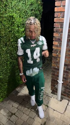 a man with dreadlocks is wearing a football uniform and standing in front of a brick wall