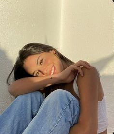 a beautiful young woman sitting on top of a wooden floor next to a white wall