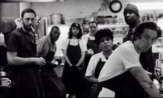 black and white photograph of people in a kitchen with one person on the counter looking at something