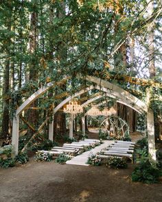 an outdoor ceremony setup with white chairs and chandelier in the middle, surrounded by trees