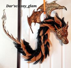 a dragon head hanging on the side of a white door with black and orange feathers