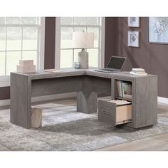 an l - shaped desk with drawers and a laptop on it in front of a window