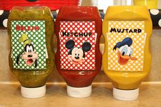 three mickey mouse cups are lined up on the kitchen counter with their lids painted yellow, red, and green