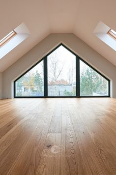 an empty room with wooden floors and skylights on the roof top, in front of a large window