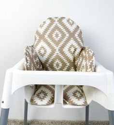 a white high chair with brown and white patterned seat covers on it's back