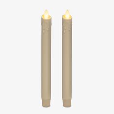 two white candles with yellow lights on each one are in front of a white background