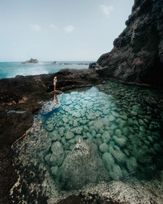 a person standing on the edge of a body of water with rocks in the background