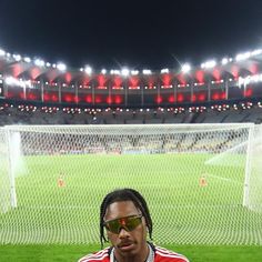 a man with dreadlocks and sunglasses sitting in front of a soccer field at night