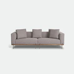 a grey couch with four pillows on it and two legs, in front of a white wall