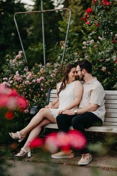 a man and woman sitting on a bench in front of flowers