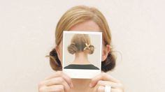 a woman is holding up a polaroid to take a selfie with her hair in a bun