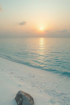 the sun is setting over the ocean and beach with rocks in the snow on the shore