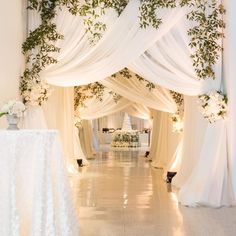 an aisle with white drapes and greenery on the ceiling, decorated with flowers