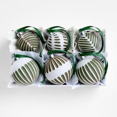 twelve white and green christmas ornaments in a cardboard box with ribbon around the edges, on a white background