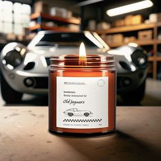 an orange candle sitting on top of a wooden table next to a white sports car