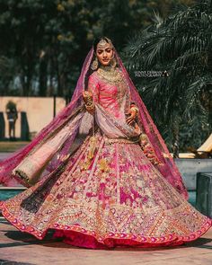 a woman in a pink and gold lehenga is standing near a pool with palm trees