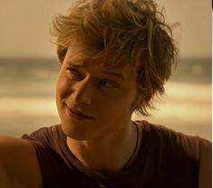 a young man standing in front of the ocean with his hair blowing in the wind