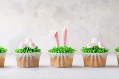 four cupcakes decorated with grass and fake bunny ears on top, sitting next to each other