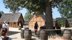 people are standing around in front of some wine barrels and buildings with thatched roofs