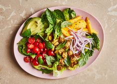 a pink plate topped with lettuce, tomato and avocado salad on top of a table