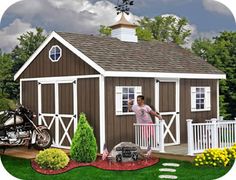 a motorcycle is parked in front of a brown shed with white doors and windows on the side