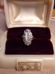 an ornate ring sits in a velvet box on a cloth covered tableclothed surface