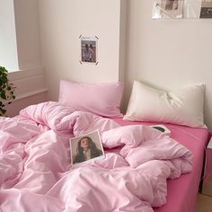 an unmade bed with pink sheets and pillows in a white room next to a potted plant