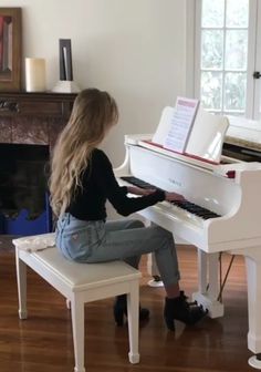 a woman sitting at a white piano in front of a fireplace