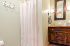 a white shower curtain in a bathroom next to a wooden vanity and toilet paper roll