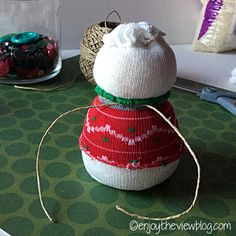 a knitted snowman ornament sitting on top of a table next to other christmas decorations