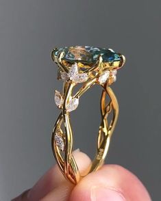 a close up of a person's hand holding a gold ring with an aqua and white diamond