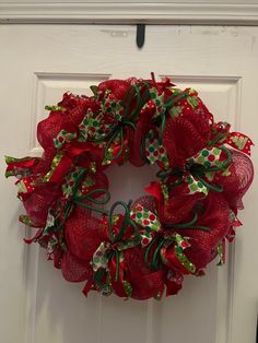 a red mesh wreath with green and white bows hanging on the front door to welcome guests