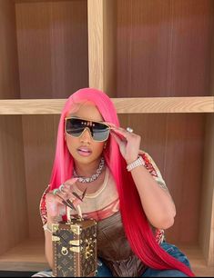 a woman with pink hair and sunglasses sitting on the floor holding a purse in front of her face