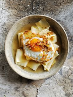 a bowl filled with pasta and an egg on top of it next to a cell phone