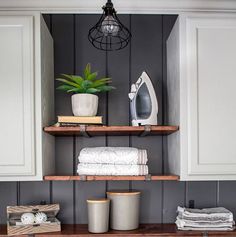 an ironing board is sitting on top of a shelf in the laundry room, next to some folded towels and a potted plant