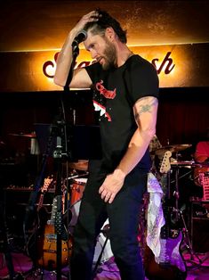 a man standing in front of a microphone with his hand on his head while singing