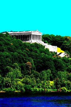 a large building sitting on top of a lush green hillside next to a lake and forest