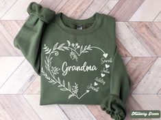 a green sweatshirt with the words grandma written in white on it, sitting on a wood floor