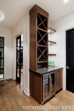 a wine rack in the corner of a room with wood floors and white walls, next to a black door