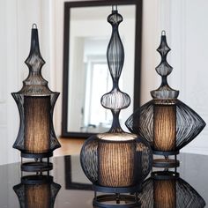 three glass vases sitting on top of a black table next to a framed mirror