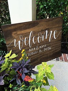 a wooden sign that says welcome next to some plants