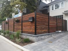 a wooden fence in front of a house on the side of a street next to a sidewalk